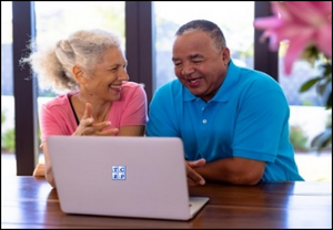 Mixed race couple sitting next to each other, smiling, and looking at a laptop screen with information about their financial retirement plan.